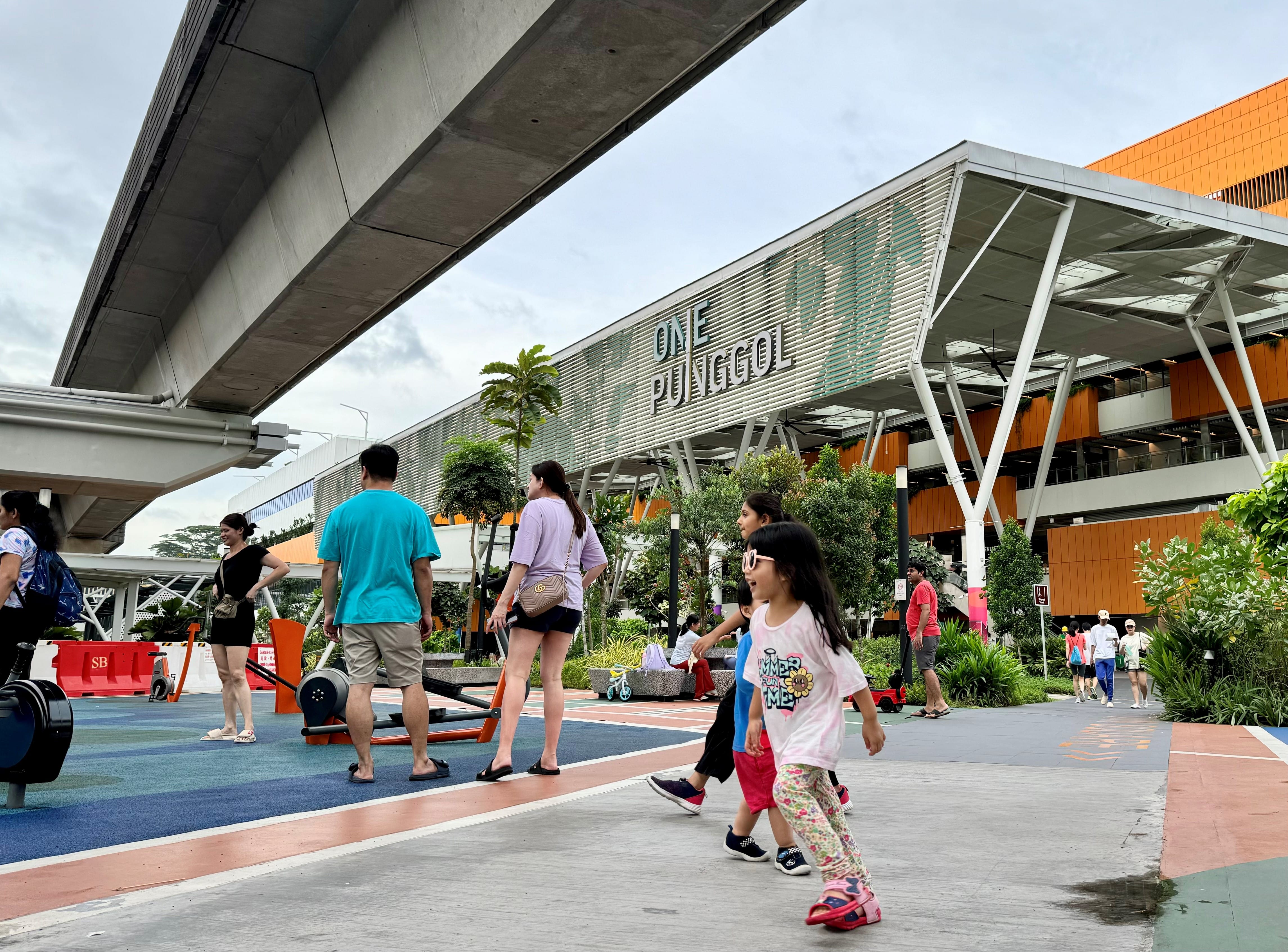 People walk and play outside the "One Punggol" building in Singapore on a cloudy day.
